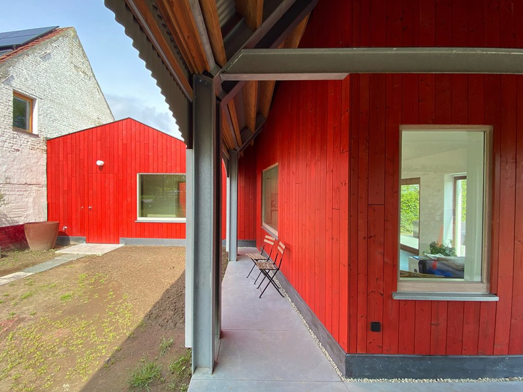 Červená fasáda nového objektu medzi domom a stodolou v Belgicku
