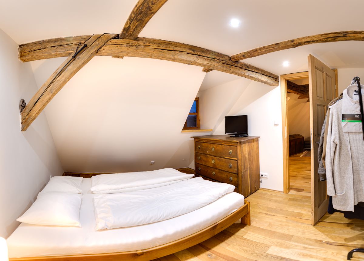 Jedna zo spální v apartmánovom dome s dvojlôžkovou drevenou posteľou, drevenou podlahou i komodou a vešiakom na oblečenie.