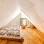 Jedna zo spální v apartmánovom dome s nízkou drevenou dvojlôžkovou posteľou, drevenou podlahou a bielymi stenami.