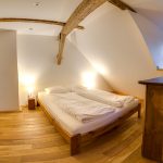 Spálňa v apatrmánovom dome s manželskou drevenou posteľou, drevenou podlahou a drevenou komodou.