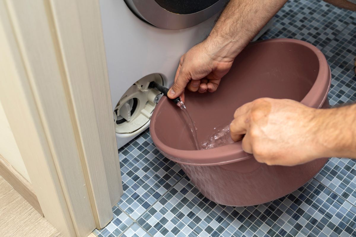 Muž vypúšťa vodu z hadice v dolnej časti práčky.