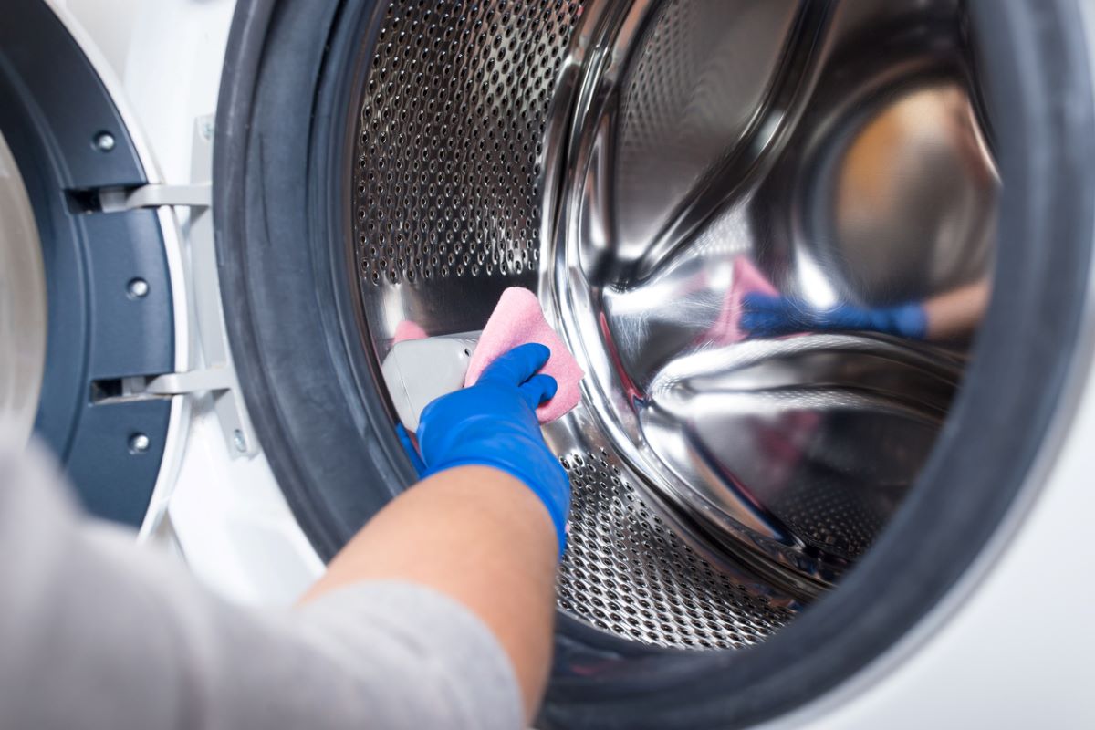 Žena čistí utierkou vnútro bubna v práčke.