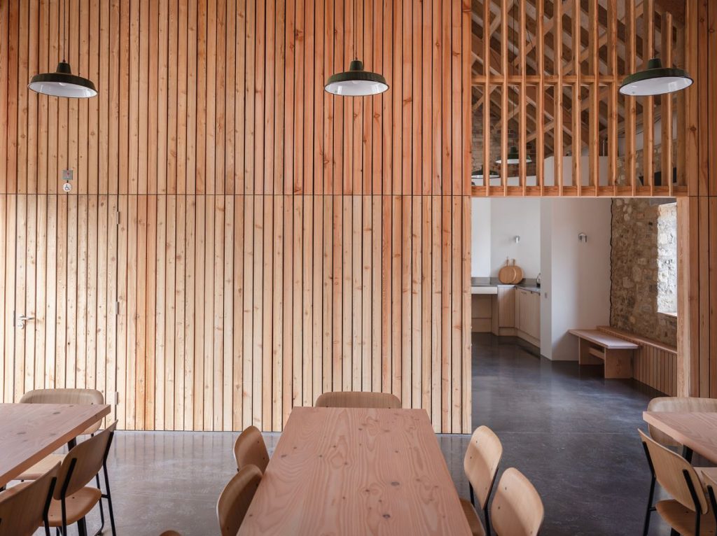 Interiér v jedenej z budov farmy s jedálenskými drevenými stolmi so stoličkami a drevom obloženými stenami.