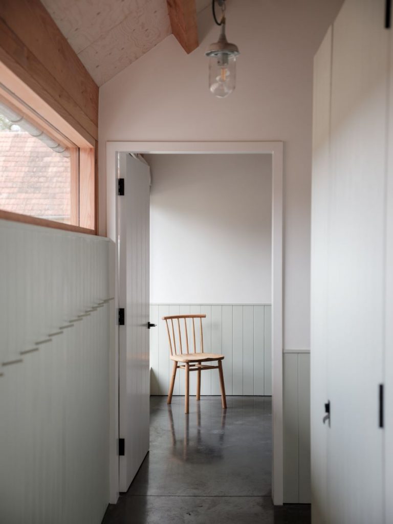 Chodba v interiéri farmy so zelenosivým obkladom stien a jednou drevenou stoličkou .