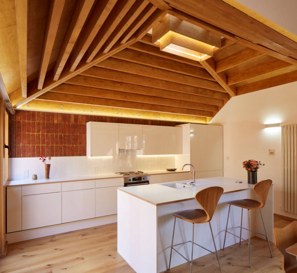 Biela kuchyňa v bungalove s drevenými vysokými stoličkami.