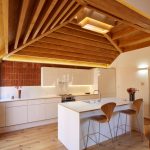 Biela kuchyňa v bungalove s drevenými vysokými stoličkami.