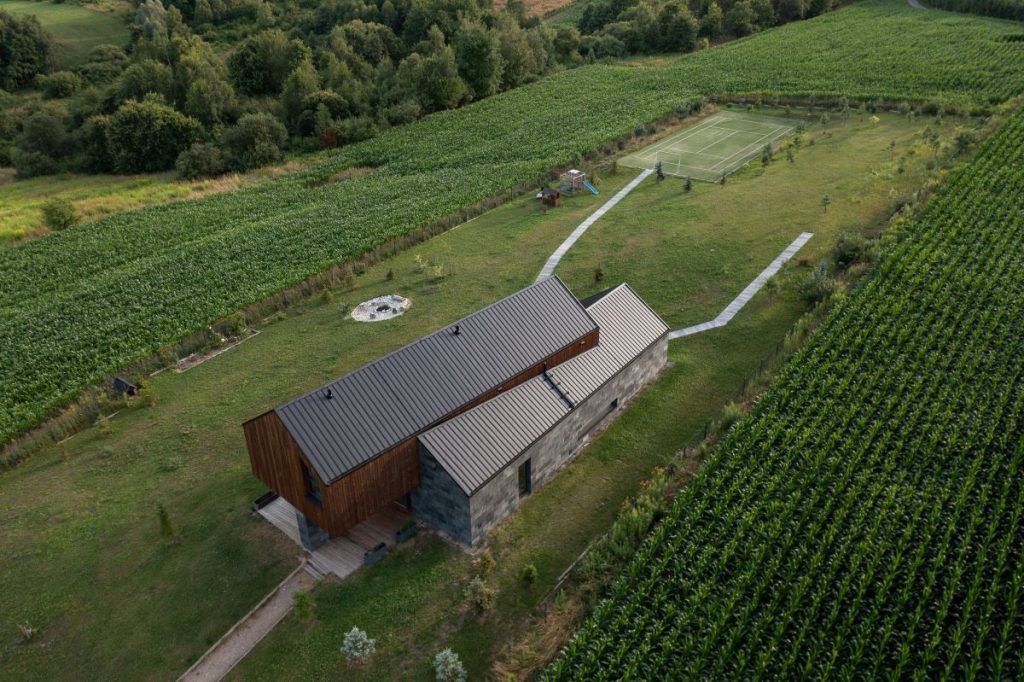 Netradičný dom na kopci v Poľsku, pohľad zhora na okolitý pozemok so športovým ihriskom, detskou šmýkačkou a kamenným ohniskom.