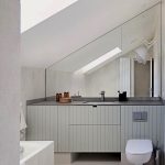 Kúpeľňa od Linea Design s veľkým lichobežníkovým zrkadlom, toaletou a skrinkou s umývadlom.