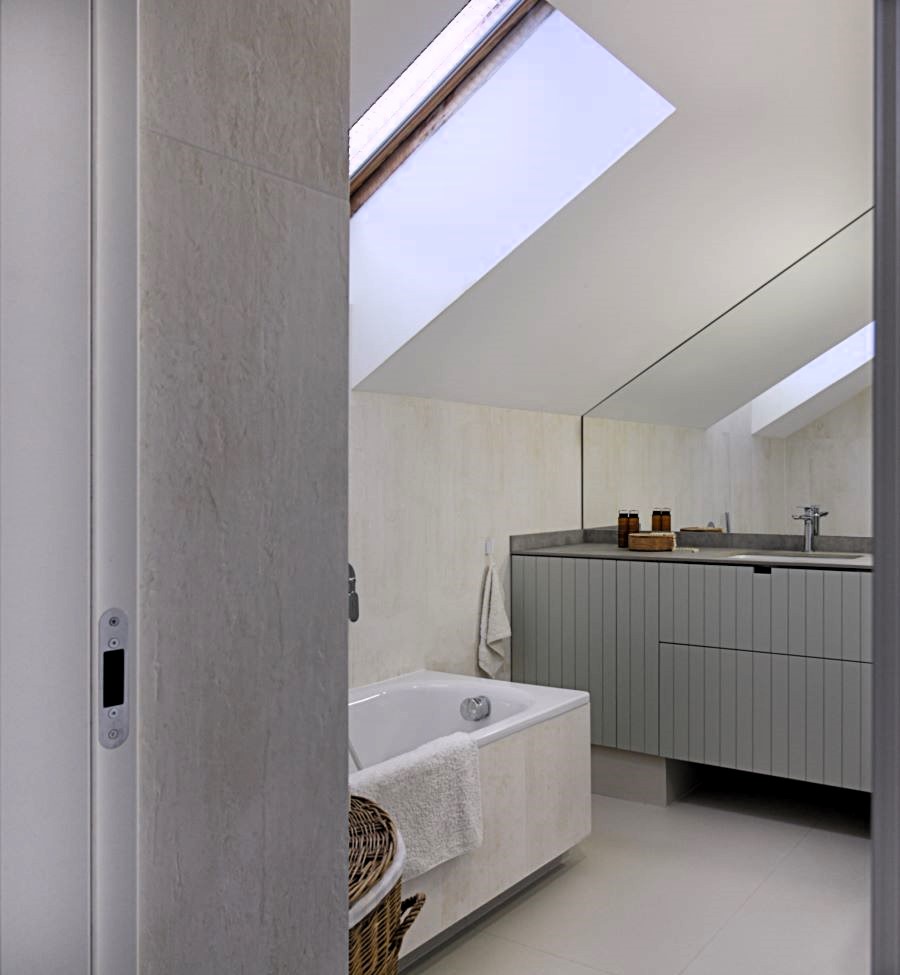 Kúpeľňa s veľkým zrkadlom, sivými skrinkami a vaňou za dverami.