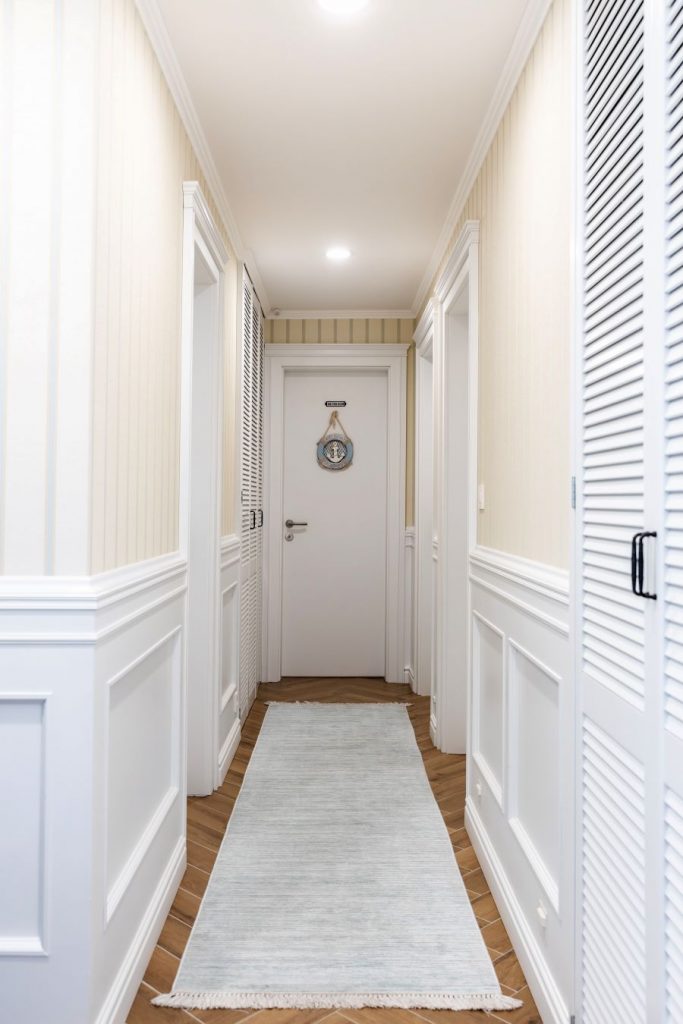 Svetlá chodba s bielymi dverami a bielym obložením stien do jednej tretiny v kombinácii so svetložltými pásikmi v modernom francúzskom vidieckom štýle.