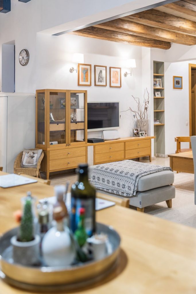 Obývačka so sivou taburetkou, vyššou presklenou vitrínkou a nižšou drevenou skrinkou pod televízor.