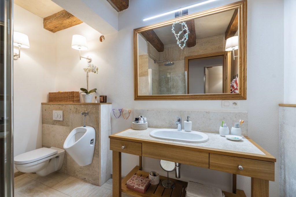 Kúpeľňa spojená s toaletou a pisoárom. Pod obdĺžnikovým zrkadlom stojí drevená skrinka s umývadlom a úložným priestorom.