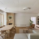 Obývačka s premietacou stenou, oválnym dreveným stolom so stoličkami, kozubom so šamotovým obkladom, svetlou sedačkou a policami na stene.