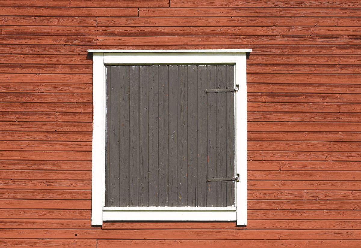 Okno s bielym rámom a tmavosivou drevenou okenicou v kontraste drevenej fasády.