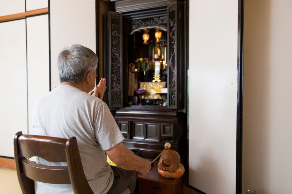 Oltár v japonskej domácnosti pred ktorým sedí starší muž.