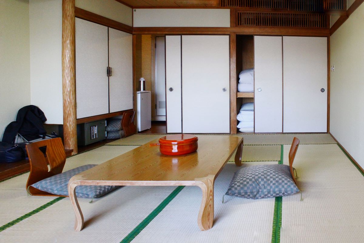 Interiér v japonskej domácnosti s nízkym dreveným stolíkom, vankúšmi na sedenie a oshiiru, skriňou na ukladanie matracov a vankúšov.