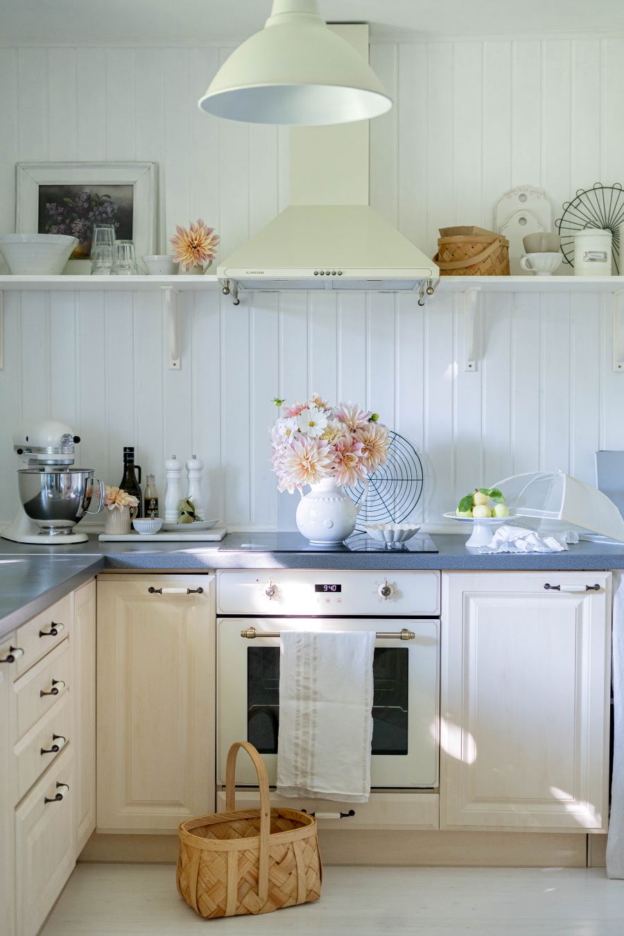 Kuchyňa v provensalskom štýle so svetlobéžovou linkou a sivou pracovnou doskou a bielym obložením na stenách. Kvety z bielej váze z džbánu uprostred.