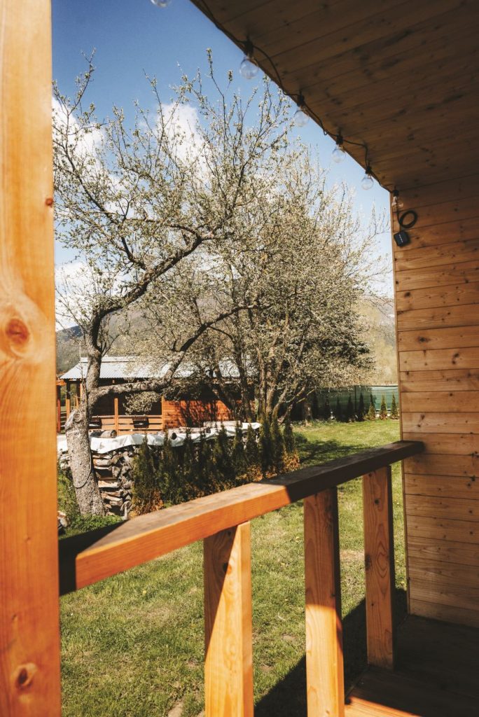 Výhľad od vstupných dverí na dvor so stromami, altánkom a naukladaným drevom.