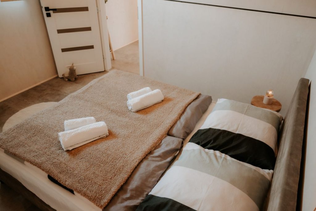 Manželská posteľ v spálni so zrolovanými bielymi uterákmi pre hostí.