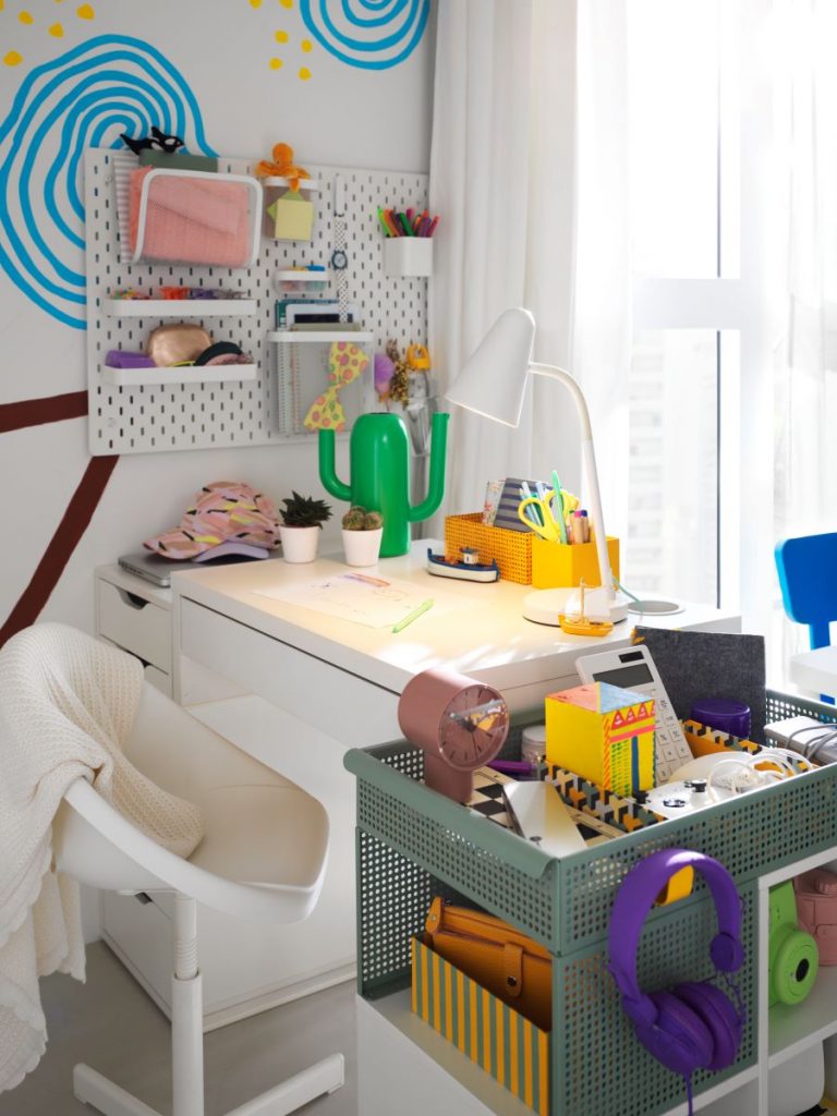 Biely písací stôl v detskej izbe s bielym perforovaným panelom a úložným "servírovacím" stolíkom po jeho pravej strane.