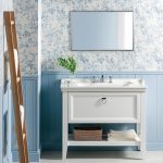 Kúpeľňa s modrým zvislým obkladom do tretiny výšky steny, vyššie kvetinový vzor na stenách. Uprostred samostatne stojace umývadlo a nad ním zrkadlo.