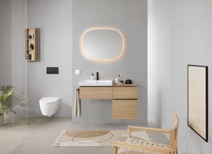 Kúpeľňa v svetlosivej farbe s frevenou skrinkou s umývadlom, oblým podsvieteným zrkadlom a toaletou.