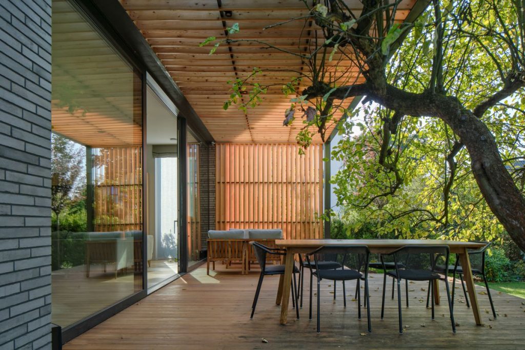 Drevená terasa domu, ktorej súčasťou je exteriérový stôl so stoličkami aj jabloň.
