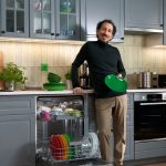Muž stojí pri otvorenej umývačke riadu v kuchyni a drží zelený tanier.