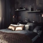 Manželská posteľ v sivočiernej miestnosti s bronzovými ozdobnými vankúšmi a bronzovou dekou.