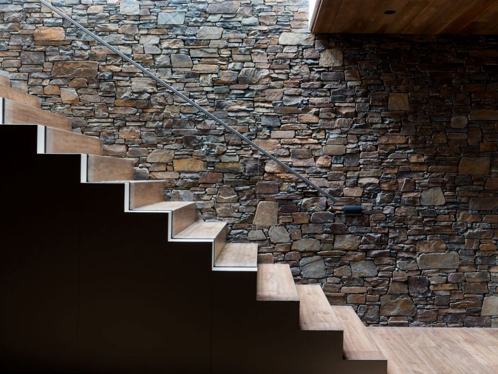 Drevené schodisko v kontraste s kamennou stenou a jednoduchým kovovým zábradlím.