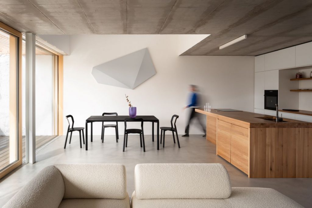 Čierny odbĺžnikový jedálenský stôl so štyrmi stoličkami vedľa kuchynskej linky v drevenom dizajne v spoločenskej časti domu.