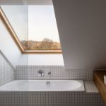 Kúpeľňa s mozaikovým obkladom v bielom prevedení a vaňou pod strešným oknom.