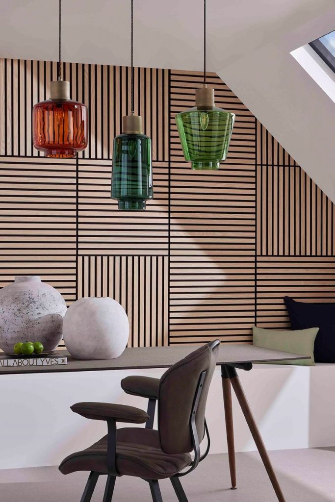 Interiér s farebnými dizajnovými svietidlami, stolom s kreslom a lamelami na stene.