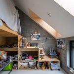 Podkrovná detská izba s dreveným nábytkom s množstvom hračiek a priznaným betónom na stenách.
