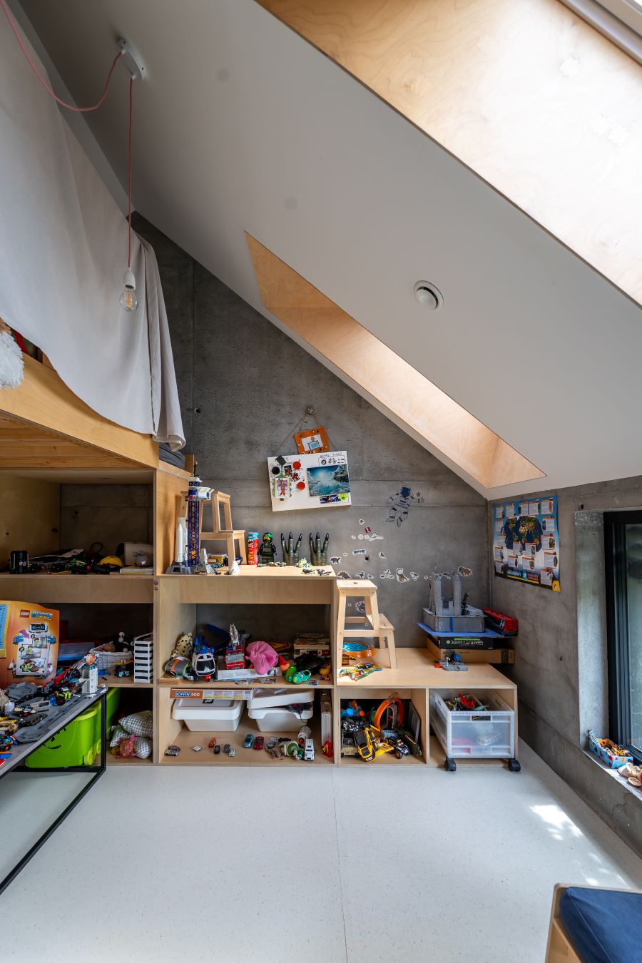 Podkrovná detská izba s dreveným nábytkom s množstvom hračiek a priznaným betónom na stenách.