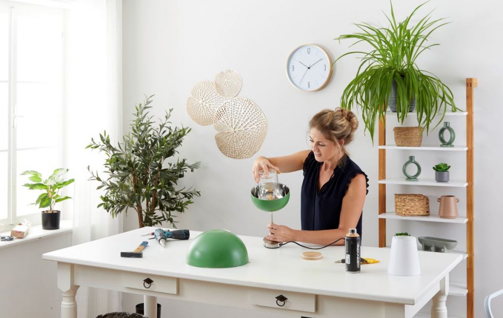 Žena pri pracovnom stole vkladá do misky so žiarovkou zaváraninový pohár.