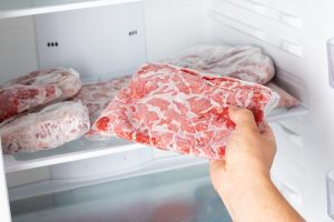 Muž vyberá zamrazené mäso v plastovom vrecku z mrazničky.