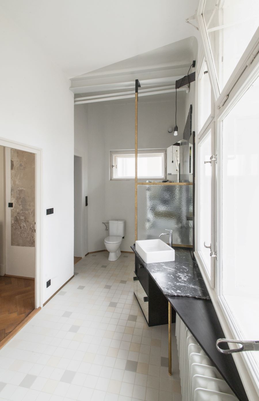 Kúpeľňa v byte, ladená do čierno-biela, s toaletou a asymetricky umiestneným umývadlom pod oknom.