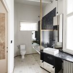 Kúpeľňa v byte s toaletou, vaňou so zrkadlovým obkladom a asymetricky umiestneným umývadlom pod oknom.