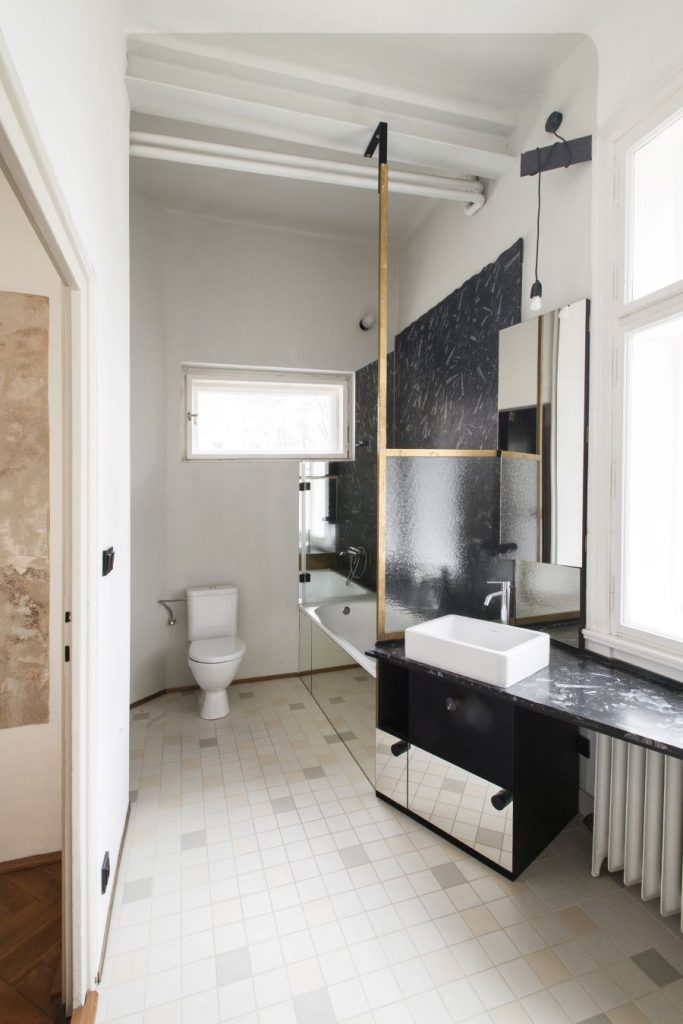 Kúpeľňa v byte s toaletou, vaňou so zrkadlovým obkladom a asymetricky umiestneným umývadlom pod oknom.
