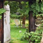 Pohľad cez starú bránu na dvor so záhradnou stoličkou.