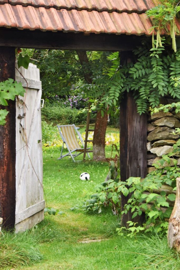 Pohľad cez starú bránu na dvor so záhradnou stoličkou.