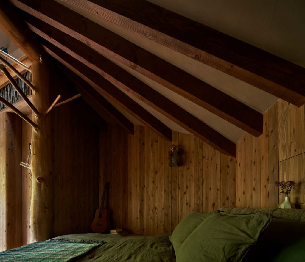 : Spálňa s manželskou posteľou a gitarou opretou v kúte chaty.