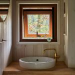 Časť kúpeľne s bielym umývadlom na drevenej masívnej doske a svetlým drevom obloženými stenami.