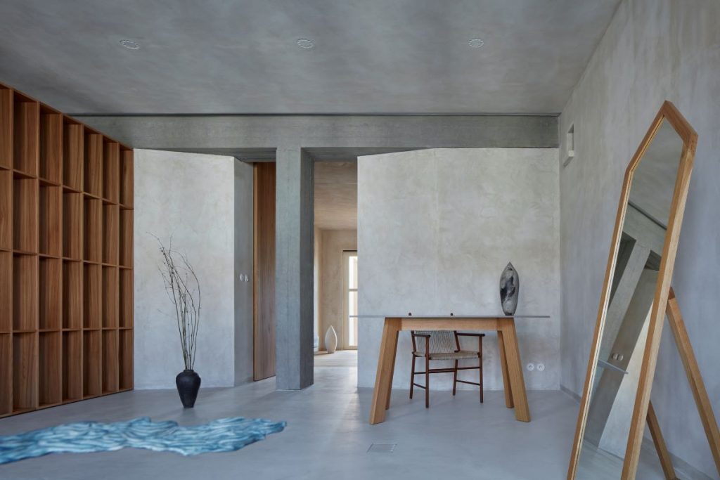 Ateliér s dreveným stolom s atypickou stoličkou, stojacím zrkadlom s dreveným rámom a policovou stenou na boku.