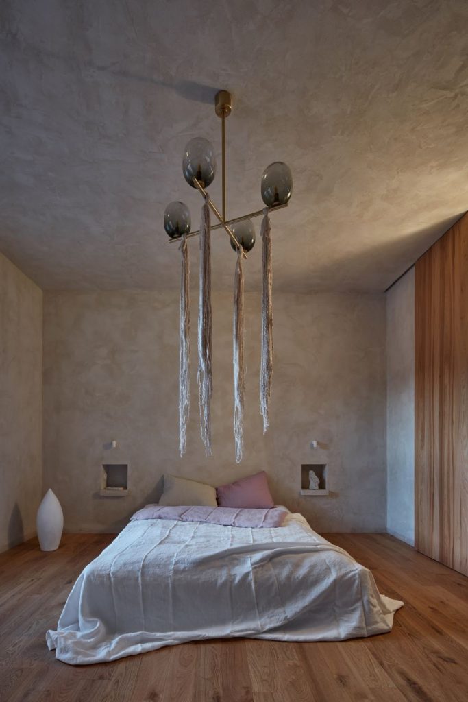 Spálňa s drevenou podlahou i časťou steny, skombinovanými s betónom. Nachádza sa v nej svietidlo, postele a dve niky, slúžiace ako odkladací priestor.