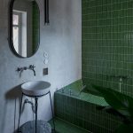 Jedna z kúpeľní v byte s vaňou obloženou zeleným obkladom, oválnym zrkadlom a atypickým umývadlom.