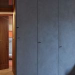 Skriňový úložný priestor na chodbe v minimalistickom dizajne s jednými otvorenými dverami, odhaľujúcimi tajný priechod do spálne.