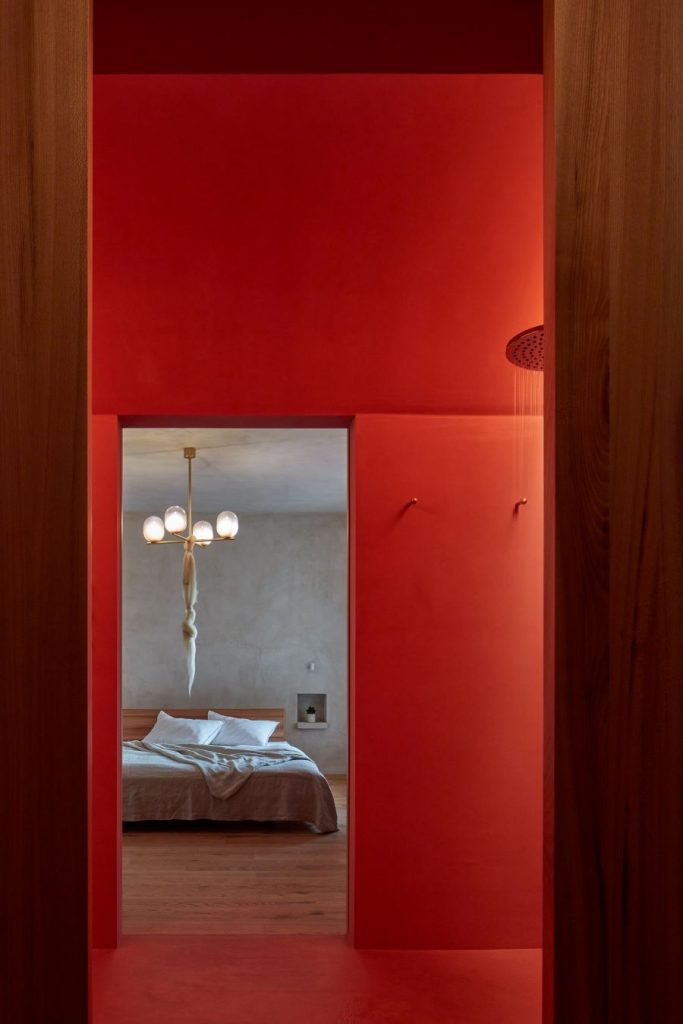 Pohľad do spálne cez dočervena sfarbenú kúpeľňu.