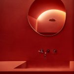 Dočervena sfarbená kúpeľňa s umývadlom a zrkadlom v nepravidelnom tvare.